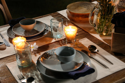 Elegant candle-lit dinner table setup with grey ceramic plates, bowls, glassware, floral decor, and warm ambient lighting for a cozy dining experience.